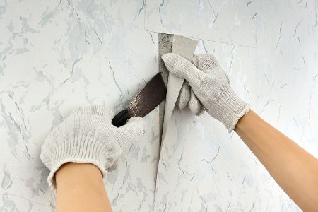 Behandschuhte Hände lösen mit einem Spachtel Tapete von der Wand