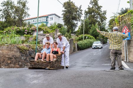 Ein Korbrodelschlitten mit zwei Touristen wird von zwei Anschiebern geschoben