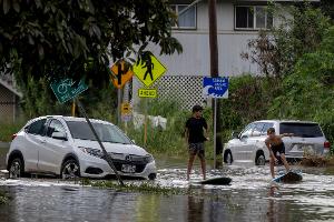 Zwei Jugendliche surfen in Waialua neben einem liegengebliebenen Fahrzeug im Hochwasser.