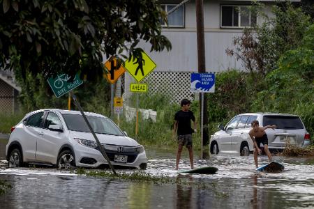 Zwei Jugendliche surfen in Waialua neben einem liegengebliebenen Fahrzeug im Hochwasser.