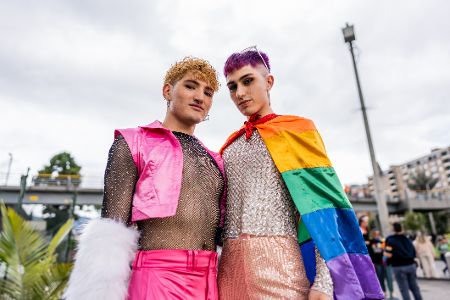 Zwei queere Personen mit Pride-Flagge auf einer Parade in der Stadt