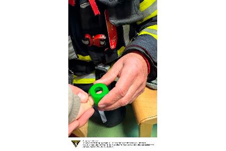 Eine Einsatzkraft der Feuerwehr München entfernt einen Holzbauklotz vom Finger eines Kindes.