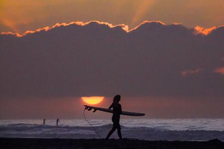 Eine Surferin trägt ihr Surfbrett in Richtung Meer.