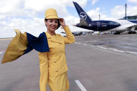 Eine Hostess trägt eine frühere Lufthansa-Uniform vor einem Passagierflugzeug der Lufthansa auf dem Flughafen Berlin-Brandenburg (BER) bei der Feier von Lufthansa zum 100. Jahrestag des Erstflugs.