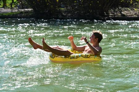 Julian treibt in einem aufblasbaren Donut im Eisbach im Englischen Garten in München. 