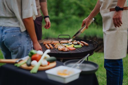 Drei Menschen stehen um einen Grill herum, auf dem gegrillt wird