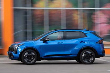 Blauer Kia Sportage 1,6 T-GDI AWD fährt seitlich durch eine urbane Umgebung, Fahrer sichtbar.