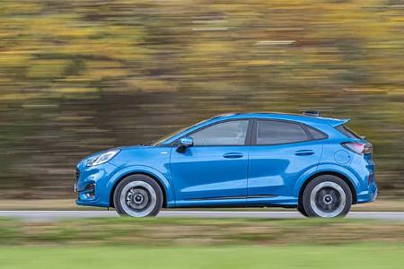 Seitenansicht eines blauen Ford Puma 1,0 EcoBoost auf einer Landstraße, aufgenommen in Bewegung.