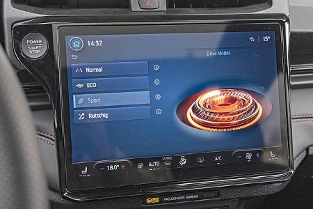 Das Bild zeigt das zentrale Infotainmentsystem eines Ford Puma 1,0 EcoBoost mit Anzeige der Fahrmodi (Normal, ECO, Sport, Rutschig). Die Bedieneinheit ist prominent im Cockpit platziert, umgeben von weiteren Bedienelementen und Lüftungsdüsen.