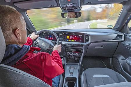 Innenaufnahme eines Opel Mokka Hybrid während der Fahrt, Blick über die Schulter des Fahrers auf das Cockpit und die Straße.