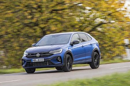 VW Taigo 1,5 TSI in blauer Lackierung fährt auf einer Landstraße, herbstliche Bäume im Hintergrund.