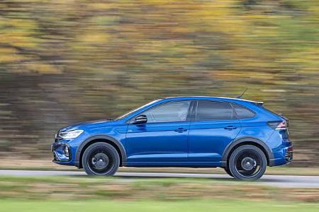 VW Taigo 1,5 TSI in Blau fährt auf einer Straße, Seitenansicht, herbstliche Umgebung im Hintergrund.