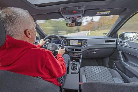 Innenaufnahme eines VW Taigo 1,5 TSI während der Fahrt, Blick über die Schulter des Fahrers auf das Cockpit und die Straße.