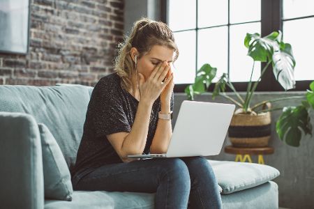 Frau mit Laptop auf dem Schoß schlägt Hände vor Gesicht zusammen