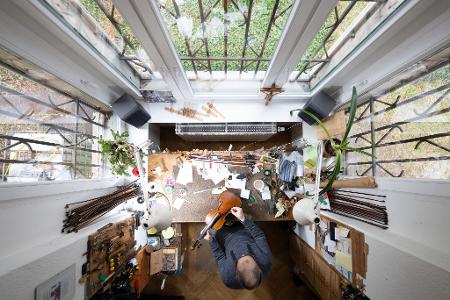 Kunsthandwerk von oben: Ein Geigenbauer arbeitet in einer Geigenwerkstatt an einer Bratsche. 