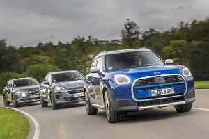 Drei Kompakt-SUVs – Cupra Terramar, Mini Countryman und Hyundai Tucson – fahren auf einer Landstraße in einer Kurve. Die Fahrzeuge sind aus der Frontperspektive zu sehen, wobei der Mini Countryman im Vordergrund fährt, gefolgt vom Cupra Terramar und dem Hyundai Tucson. Die Szene spielt bei bewölktem Himmel und grüner Umgebung.