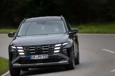 Hyundai Tucson 1.6 T-GDI fährt auf einer Landstraße in einer Kurve, Frontansicht, Tagfahrlicht eingeschaltet.