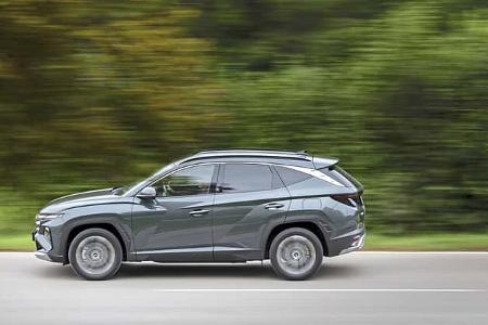 Hyundai Tucson 1.6 T-GDI fährt auf einer Landstraße, Seitenansicht, grüner Hintergrund.