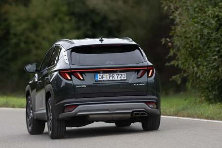 Hyundai Tucson 1.6 T-GDI SUV auf einer Landstraße, Heckansicht, fahrend, mit sichtbarem Auspuff und Rückleuchten.