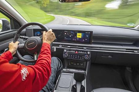 Innenraumaufnahme eines Hyundai Tucson 1.6 T-GDI während der Fahrt, Fokus auf Cockpit und Fahrer.