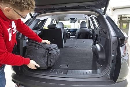 Ein Mann lädt eine schwarze Tasche in den Kofferraum eines Hyundai Tucson 1.6 T-GDI. Die Rücksitze sind umgeklappt, der Laderaum ist vergrößert.