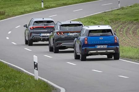 Drei Fahrzeuge – Cupra Terramar, Mini Countryman und Hyundai Tucson – fahren hintereinander auf einer Landstraße durch eine grüne Landschaft. Die Fahrzeuge sind von hinten zu sehen, jedes Modell ist deutlich erkennbar.