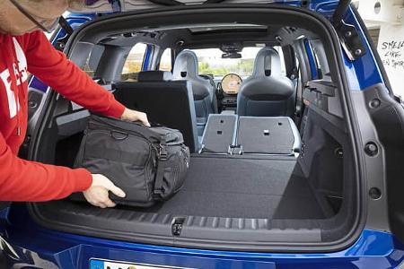Kofferraum des Mini Countryman C 2,0 mit umgeklappter Rückbank, Person lädt schwarze Tasche ein.