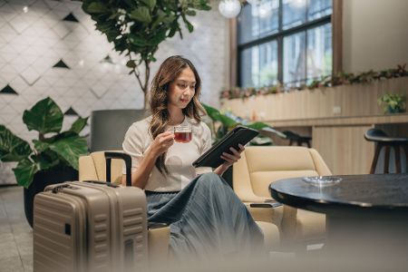 Frau sitzt in Flughafenlobby mit Tee und einer Zeitschrift