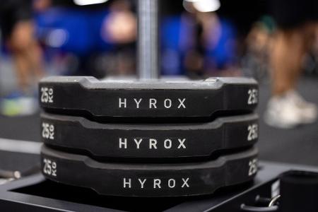 Hantelscheiben mit dem Schriftzug Hyrox an einem Messestand, wo wenig später ein Lauf- und Workout-Wettbewerb stattfinden sollte.