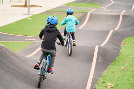 Kids riding a bike on a concrete pumptrack.