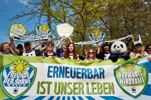 Demonstrierende halten ein Banner und Schilder in die Höhe, darunter eine Person im Pandakostüm.