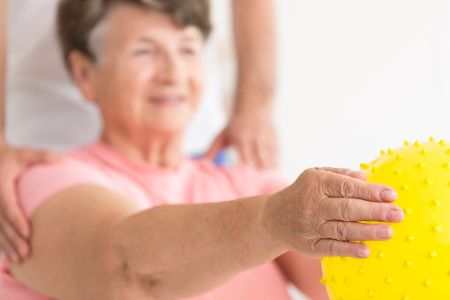 Ältere Frau hält unter Aufsicht eines Pflegers einen Ball