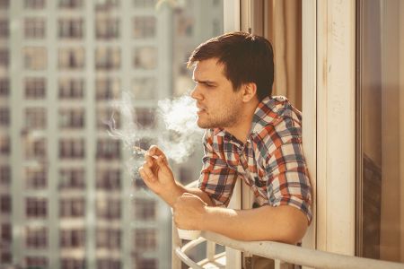 Mann steht auf Balkon und raucht Zigarette