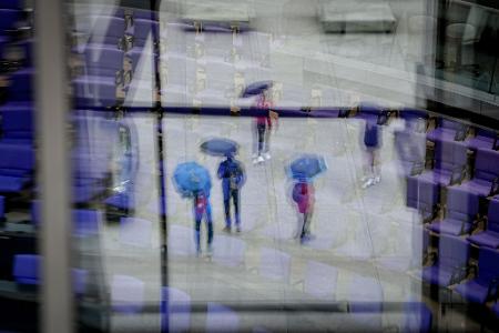 Passanten mit Regenschirmen spiegeln sich in den Fenstern vor dem Plenarsaal des Bundestags.