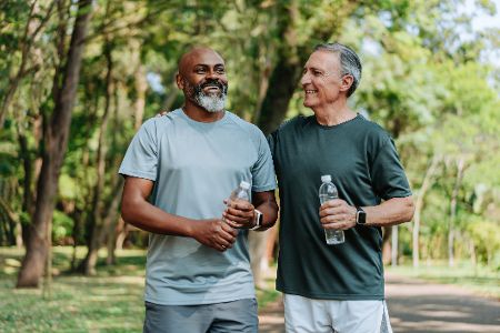 Älterer weißer Mann und älterer schwarzer Mann mit Wasserflasche in der Hand beim Sport im Park