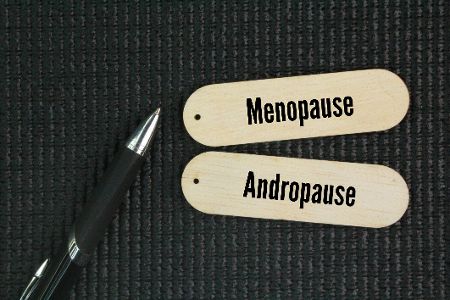 Zwei Schilder mit der Beschriftung Menopause und Andropause liegen neben einem Stift