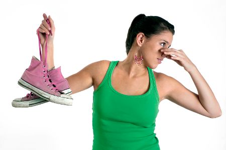 Junge Frau hat in der einen Hand stinkende Schuhe und hält sich mit der anderen die Nase zu