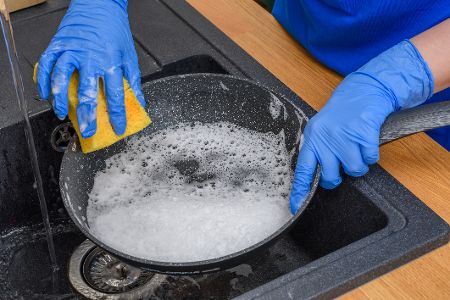 Hände mit Gummihandschuhen schrubben einen Topf