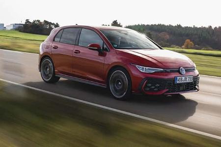 VW Golf GTI in Rot fährt auf einer Landstraße durch ländliche Umgebung.