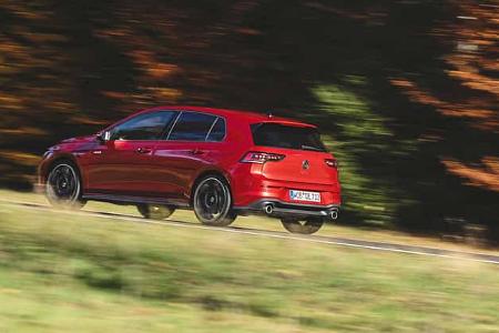 Roter VW Golf GTI (Modell RG25) fährt auf einer Landstraße, herbstliche Bäume im Hintergrund, Bewegungseffekt.