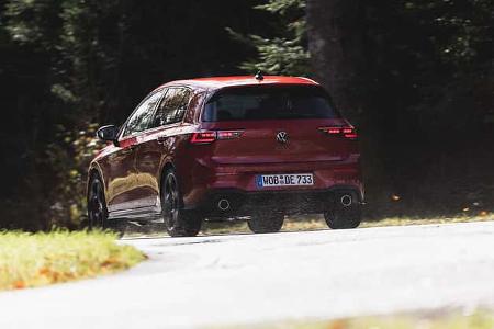 VW Golf GTI auf Landstraße, Heckansicht, rote Lackierung, fahrend, ländliche Umgebung.