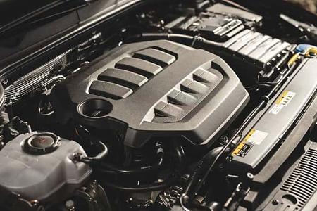 Detailaufnahme des Motorraums eines VW Golf GTI der Baureihe RG25, Modelljahr nicht explizit genannt, aber durch Dateiname und sichtbare Technik erkennbar. Der Motorblock ist mit einer großen Kunststoffabdeckung versehen, diverse Komponenten wie Kühlmittelbehälter und Kabelstränge sind sichtbar.