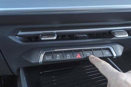 Detailaufnahme der Mittelkonsole eines Audi Q3 SUV TFSI quattro mit Bedienfeld und Finger, der eine Taste betätigt.