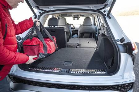 Audi Q3 SUV TFSI quattro mit geöffnetem Kofferraum, ein Mann legt eine rote Tasche hinein. Die Rücksitze sind teilweise umgeklappt, um das Ladevolumen zu vergrößern.