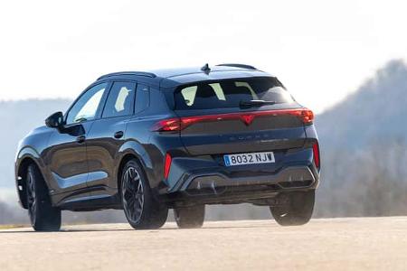 Das Bild zeigt einen Cupra Terramar 2.0TSI 4Drive aus der Heckperspektive auf einer asphaltierten Fahrbahn. Das Fahrzeug ist in Bewegung und hebt leicht ab, im Hintergrund sind unscharfe Hügel erkennbar.