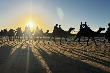Menschen reiten auf Kamelen am Birubi Beach nördlich von Newcastle in Australien.