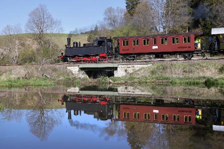Eine Dampflokomotive ist auf der Schwäbischen Alb unterwegs und spiegelt sich in einem Gewässer.