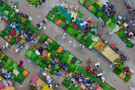Eine Luftaufnahme zeigt das lebhafte Treiben auf einem Gemüsemarkt in Ahmedabad in Indien, wo Verkäufer frische Produkte anordnen und Kunden sich durch die engen Marktgassen bewegen.