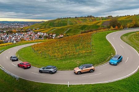 Fünf Elektro-SUVs (Hyundai IONIQ 5, VW ID.4 Pro, Opel Grandland, Kia EV6, Renault Scenic E-Tech Electric) fahren auf einer kurvigen Landstraße durch Weinberge. Die Aufnahme stammt von einer Drohne und zeigt die Fahrzeuge in einer engen Serpentine mit Blick auf eine Ortschaft und herbstliche Weinberge.