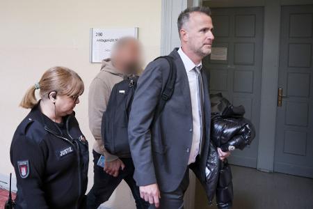 Der Zeuge (Mitte des Bildes) wird von seinem Anwalt (rechts im Bild) in den Gerichtssaal begleitet.